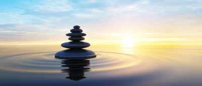 Stack of stones in water in front of a sunset illustrating the concept of managing stress and anxiety.