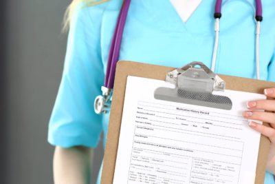 Female doctor holds medication history form on clip board, showing importance of medication management in primary care.