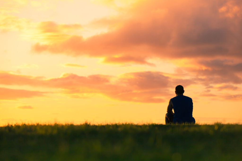 Man sits silhouetted by the setting sun, illustrating the importance of men’s mental health.