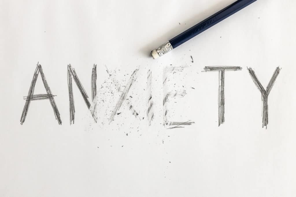 Anxiety written on white paper with a pencil, partially erased with an eraser. Picture shows importance of managing anxiety.