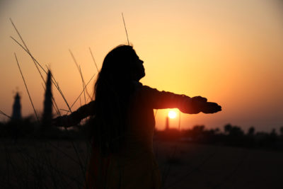 Woman practices calming techniques, silhouetted against a sunset.