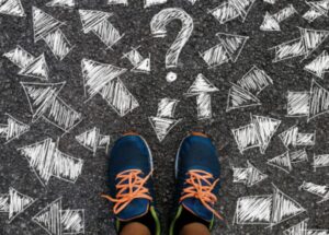 Photo of feet in blue and orange sneakers standing on chalk drawings of arrows illustrating many choices in psychologist vs psychiatrist.
