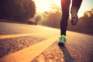 Legs and brightly colored sneakers of a woman athlete running on a road, illustrating whether running helps anxiety