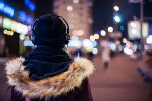 Woman wearing headphones, winter hat and jacket, on city street at night, reflecting how people may experience depression and anxiety differently. 