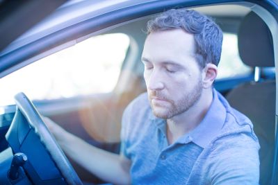 Man with eyes closed sitting in a car, indicating the isolation and mental health issues brought on by COVID