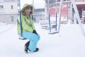 Young woman in snow gear stitting on a swing in a snowy playground representing how winter can impact Seasonal Affective Disorder