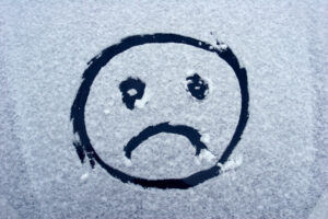 An unhappy smiley face drawn on a snow covered windshield representing a symptom of seasonal affective disorder
