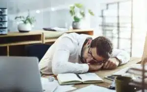 Young businessman sleeps at his desk in an office showing how people make take naps for anxiety.