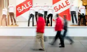 Men walk by a window display with “sale” prominently displayed, showing how holiday overspending may impact to our mental health