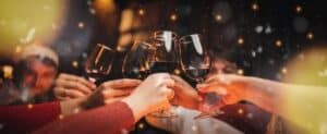 Friends toast with red wine at a holiday party, showing risk of holiday indulgence in food and drink