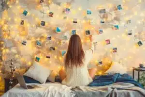 Girl puts up pictures from years gone by on wall with Christmas lights showing how nostalgia may lead to holiday overspending