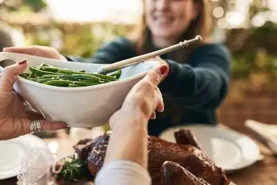 Woman passes green beans, showing how important it is to cope with family anxiety around the holidays