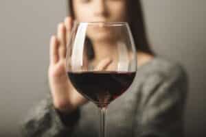 Foreground picture of red wine with woman holding up hand to say, illustrating holiday indulgence may impact mental health.