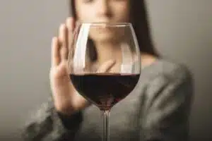 Foreground picture of red wine with woman holding up hand to say, illustrating holiday indulgence may impact mental health.