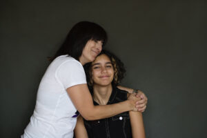 mixed-race non-binary teenager being hugged by their supportive mother indicatiing the importance of a safe and loving home for LGBTQ+ teenagers