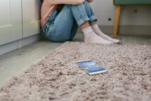 Young woman with head on knees and phone in foreground representing the stresses of cyberbullying