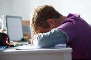 Young white boy with head on keyboard indicating feelings of anxiety and depression due to cybrebullying