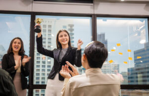 Young Asian woman holding up a trophy in an office representing the model minority myth 