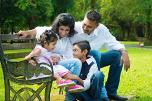 Happy Indian family at outdoor park. Candid portrait of parents and children having fun at garden park.