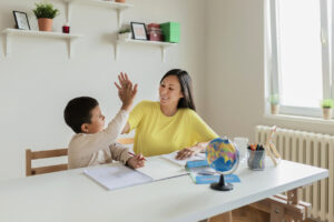 Asian mother and son sharing a high five while working on homework at home, indicating ways parents can help ease their children’s back to school anxieties.