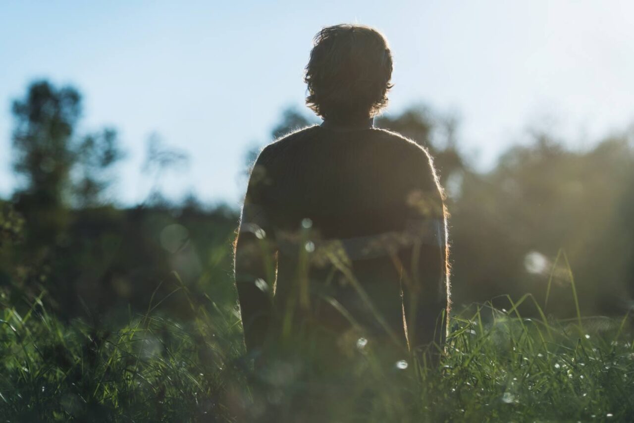 Image of a man in silhouette from behind standing in a field, being in nature to relieve anxiety.