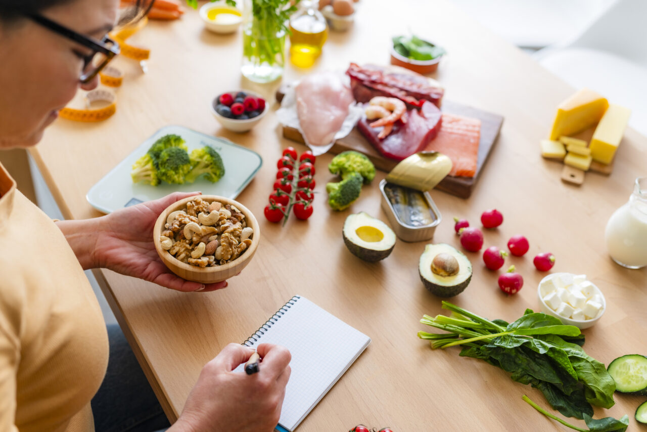 Mature woman planning a healthy low carb diet. She is taking notes of the right portion of food. Holding nuts and seeds and writing