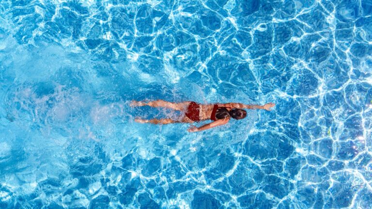 Young woman aerial drone view from above, swimming in blue water for relaxation and mental health